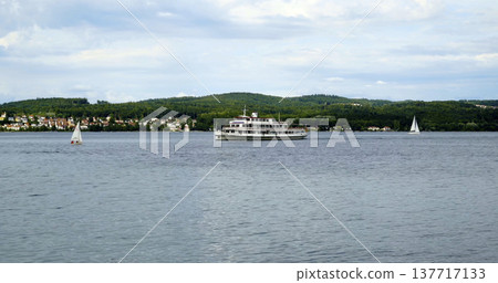 Large boat sails on lake with small sailboats nearby at afternoon under cloudy sky in a scenic location Large boat sails on lake with small sailboats nearby at afternoon under cloudy sky in a scenic location 137717133