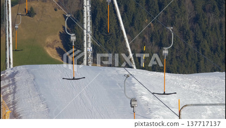 Ski lift in operation on a snowy mountain with a clear sky and green grass in the background during winter Ski lift in operation on a snowy mountain with a clear sky and green grass in the background during winter 137717137