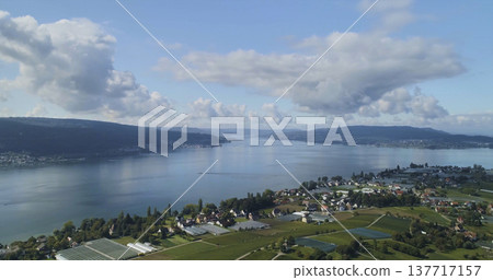 Sky view of a lake surrounded by green fields and small houses in the countryside near a town during daytime Sky view of a lake surrounded by green fields and small houses in the countryside near a town during daytime 137717157