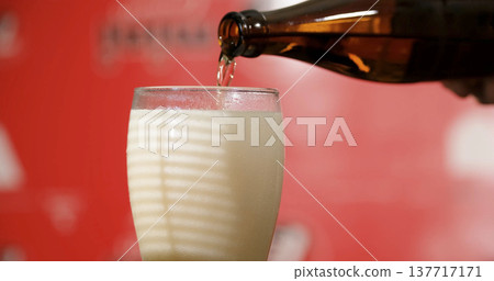 Pouring a drink into a glass at a gathering in a lively setting with a red background and bright lighting Pouring a drink into a glass at a gathering in a lively setting with a red background and bright lighting 137717171