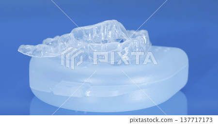 Clear dental retainer on a storage case with a blue background during the daytime in a dental office 137717173