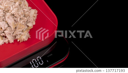 Weighing shredded chicken on a digital kitchen scale in a kitchen setting at midday 137717193