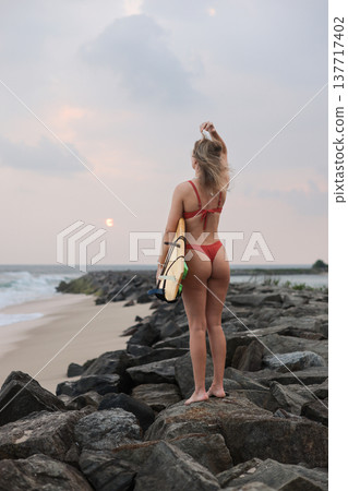 Morning Ocean Tranquility. Serene Dawn Setting With Solitary Surfer On Rocky Coast Under Soft Pastel Sky 137717402