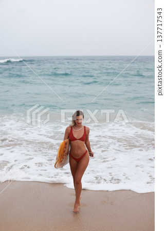 Passionate Surfer Exiting Ocean Shore Carrying Cheerful Yellow Surfboard And Wearing Lively Red Bikini 137717543