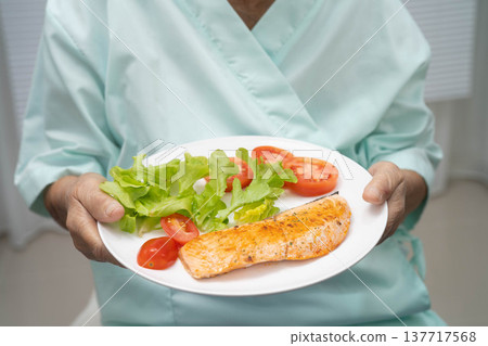 Asian elderly woman patient eating salmon stake and vegetable salad for healthy food in hospital. Asian elderly woman patient eating salmon stake and vegetable salad for healthy food in hospital. 137717568