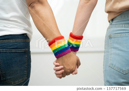 Asian LGBT couple woman holding hand wearing rainbow wristband. 137717569