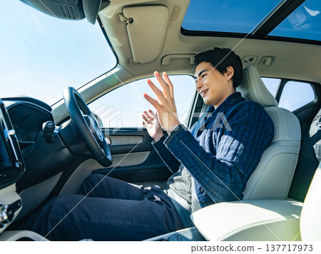 一名男性駕駛員在汽車駕駛座上使用免持駕駛。 一名男性駕駛員在汽車駕駛座上使用免持駕駛。 137717973