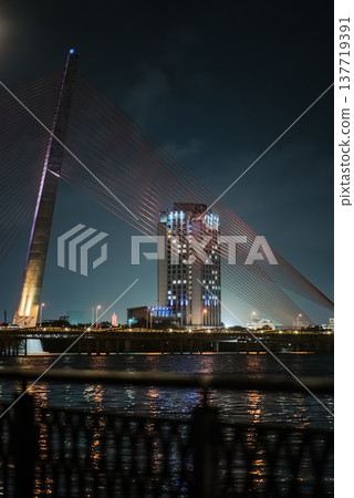 Cable-stayed bridge over Han River in Da Nang illuminated at night with city skyline reflections, Modern suspension bridge architecture across in Danang, evening cityscape with lights Cable-stayed bridge over Han River in Da Nang illuminated at night with city skyline reflections, Modern suspension bridge architecture across in Danang, evening cityscape with lights 137719391
