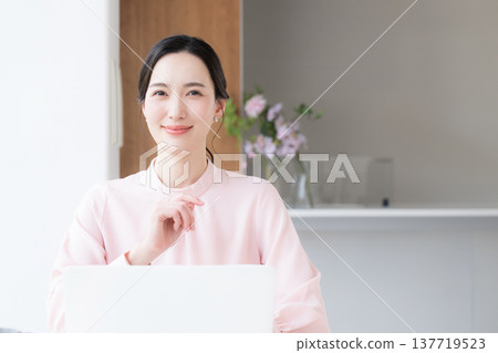 一位身穿粉紅色洋裝的美麗女子坐在辦公桌前使用電腦,直視鏡頭。 一位身穿粉紅色洋裝的美麗女子坐在辦公桌前使用電腦,直視鏡頭。 137719523
