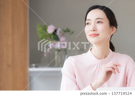 一位身穿粉紅色洋裝的美麗女子坐在辦公桌前使用電腦工作。 137719524
