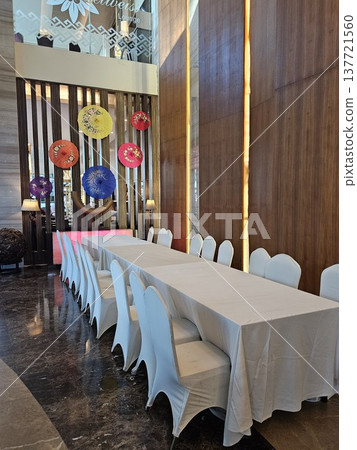 An elegant banquet setup featuring a long dining table with white tablecloths and chair covers, set against a modern interior wall decorated with vibrant 137721560