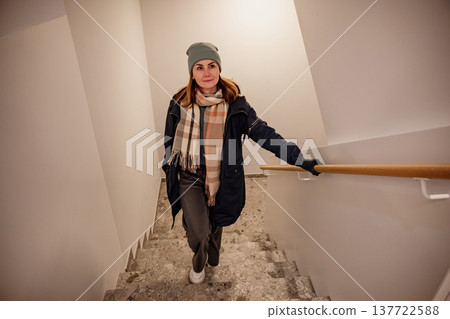 Woman walking down stairs wearing a scarf and a beanie during the winter season Woman walking down stairs wearing a scarf and a beanie during the winter season 137722588