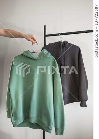 Hand holding two hoodies on display in a clothing shop during the day Hand holding two hoodies on display in a clothing shop during the day 137722597