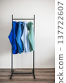 Different colored hoodies hanging on a rack in a room with light walls and wooden floor 137722607
