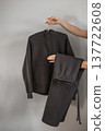 A person holds a black zip-up sweater and matching pants in a simple indoor setting during daytime 137722608