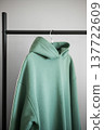 Green hoodie hanging on a black rack in a simple room with plain walls 137722609