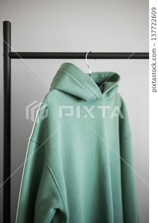 Green hoodie hanging on a black rack in a simple room with plain walls Green hoodie hanging on a black rack in a simple room with plain walls 137722609