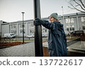 Woman stands by a lamp post in a city area during winter, looking around 137722617