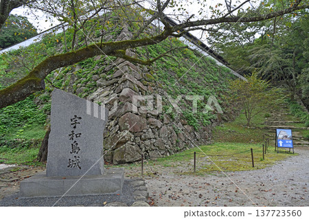 A view of the entrance to the castle path, surrounded by a stone monument marking the existing keep of Uwajima Castle and high stone walls that evoke a sense of history. A view of the entrance to the castle path, surrounded by a stone monument marking the existing keep of Uwajima Castle and high stone walls that evoke a sense of history. 137723560