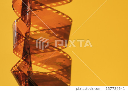 Film strip, twisted and unrolled, creating spiral shape on an orange yellow background Film strip, twisted and unrolled, creating spiral shape on an orange yellow background 137724641