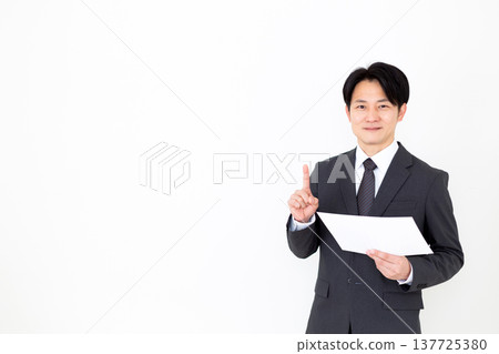 A middle-aged businessman in a suit holds up his index finger while looking at a graph. A middle-aged businessman in a suit holds up his index finger while looking at a graph. 137725380