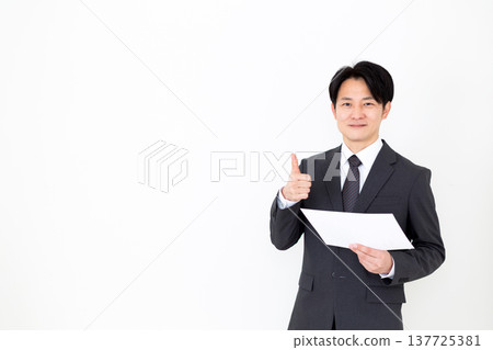 A middle-aged businessman in a suit gives a thumbs-up while looking at a graph. 137725381