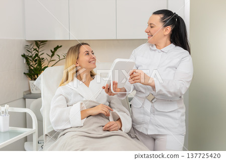 Middle-aged woman smiling in mirror after cosmetic procedure in clinic with visible skin results 137725420
