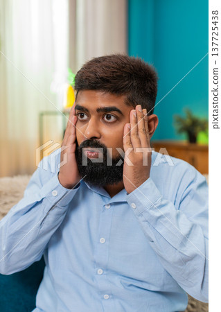 Indian man holds head eyes wide panic overload stress reaction severe pressure mental strain indoors Indian man holds head eyes wide panic overload stress reaction severe pressure mental strain indoors 137725438