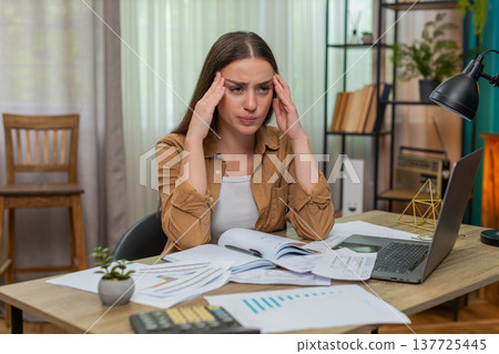 Young woman head in hands staring at overdue bills calculator and laptop wondering how she will pay 137725445