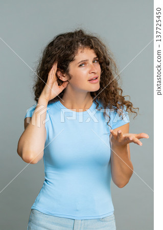 Woman holding hand near ear gesture listening carefully indicating cannot hear confused reaction 137725450