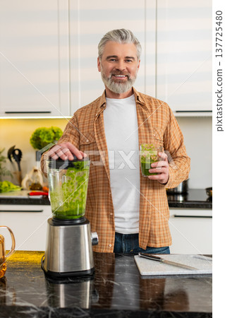 Middle-aged man drinking fresh green smoothie after blender prep for healthy diet in modern kitchen Middle-aged man drinking fresh green smoothie after blender prep for healthy diet in modern kitchen 137725480