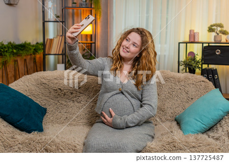 Pregnant woman taking selfie with baby bump on smartphone smiling gently touching belly at home Pregnant woman taking selfie with baby bump on smartphone smiling gently touching belly at home 137725487