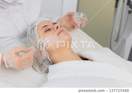 Enzyme therapy, beautician applying moisturizing medical cream on young woman face with brushes 137725488
