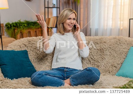 Adult woman arguing on smartphone at home, waving hands nervously with anger and expressive emotion 137725489