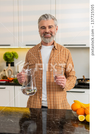 Middle-aged man drinking water in kitchen for healthy diet hydration weight loss lifestyle at home 137725505