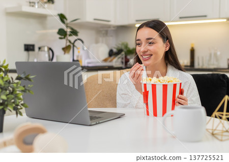 Young woman enjoys trailer laughs with popcorn laptop nearby cozy night fun video watch streaming Young woman enjoys trailer laughs with popcorn laptop nearby cozy night fun video watch streaming 137725521