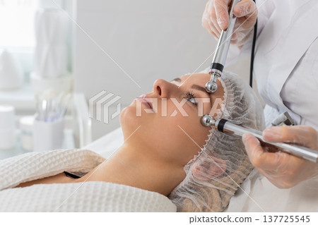 Adult woman receives rejuvenating facial therapy in cosmetology clinic by professional cosmetologist Adult woman receives rejuvenating facial therapy in cosmetology clinic by professional cosmetologist 137725545