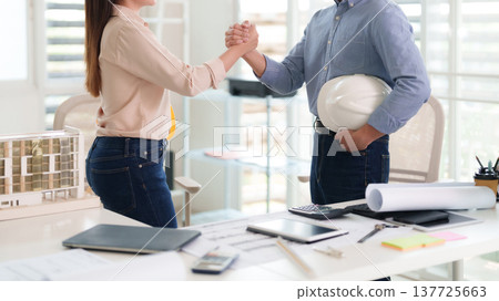 Asian adult architects engineers shaking hands project success collaboration partnership agreement professional teamwork at modern construction planning office workspace Asian adult architects engineers shaking hands project success collaboration partnership agreement professional teamwork at modern construction planning office workspace 137725663
