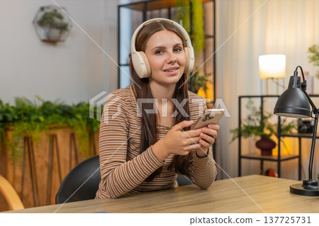 Young woman in headphones listens to productivity podcast and writes ideas on smartphone for tasks Young woman in headphones listens to productivity podcast and writes ideas on smartphone for tasks 137725731