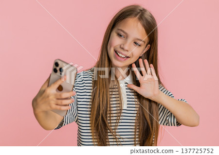 Child girl kid happily receiving video call on smartphone joyfully waving and talking with friend Child girl kid happily receiving video call on smartphone joyfully waving and talking with friend 137725752