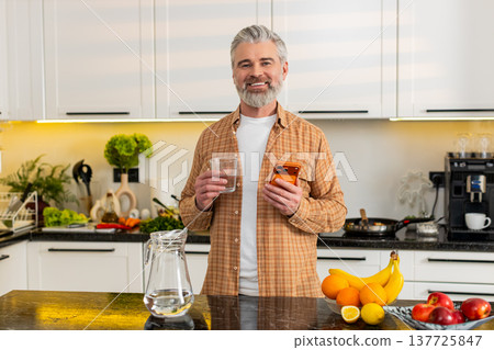 Middle-aged man checks smartphone while drinking water in kitchen for healthy diet hydration routine Middle-aged man checks smartphone while drinking water in kitchen for healthy diet hydration routine 137725847