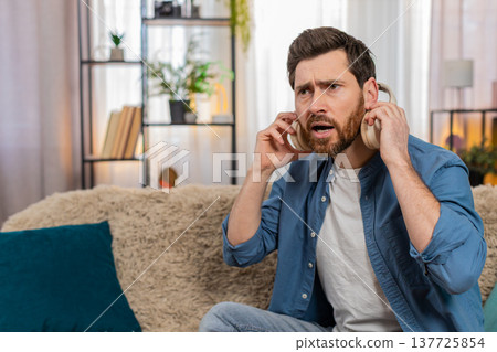 Man in headphones suddenly takes them off looking surprised reacting to strange unexpected sound 137725854