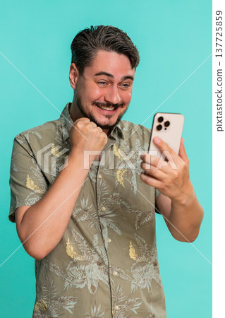 Adult man clenches fist with joy while looking at smartphone celebrating victory good news reaction 137725859