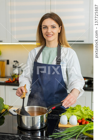 Middle-aged woman stirring hot soup in kitchen smiling healthy diet cooking for weight loss wellness 137725887