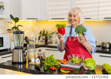 Senior old woman smiling in kitchen choosing fresh vegetables for healthy diet and home cooking meal Senior old woman smiling in kitchen choosing fresh vegetables for healthy diet and home cooking meal 137725908