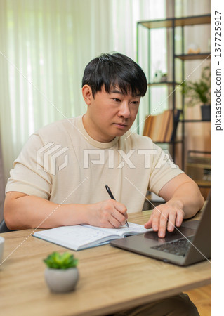 Asian man taking notes from online course on laptop, explaining to camera with clear confident tone 137725917
