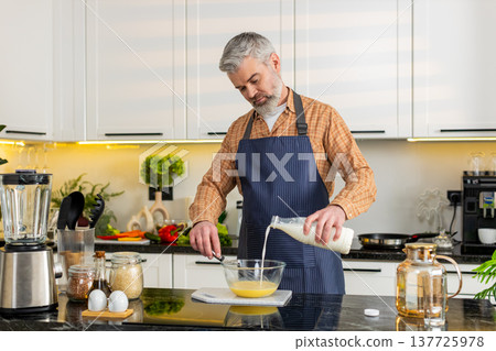 Middle-aged man whisking eggs with milk in home kitchen preparing healthy breakfast recipe for diet Middle-aged man whisking eggs with milk in home kitchen preparing healthy breakfast recipe for diet 137725978