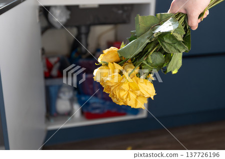 Woman throwing away a bouquet of withered yellow roses into a kitchen bin. End of holiday concept. Sadness and separation after a celebration. Decluttering and cleaning a messy home. photography 137726196