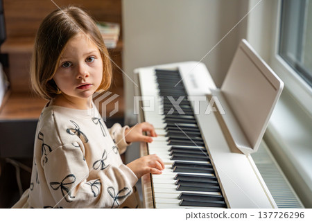 Home lesson on music for the girl on white piano synthesizer. Concept of early development: learning music enhances motor skills, hearing, and intelligence, fostering creativity from childhood 137726296