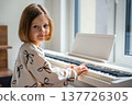 Home lesson on music for the girl on white piano synthesizer. Concept of early development: learning music enhances motor skills, hearing, and intelligence, fostering creativity from childhood 137726305